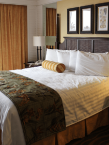 Ein gemachtes Bett in einem Hotellzimmer mit einem gelb gestreiften zylinderförmigem Poslster und einer Steppdecke