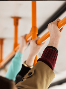 Mehrere Hände halten sich bei einer orangen Haltestange in einem Bus an.