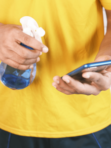 Eine Person mit einem gelben T-Shirt sprüht ein Smartphone-Display mit SC-Wasser an